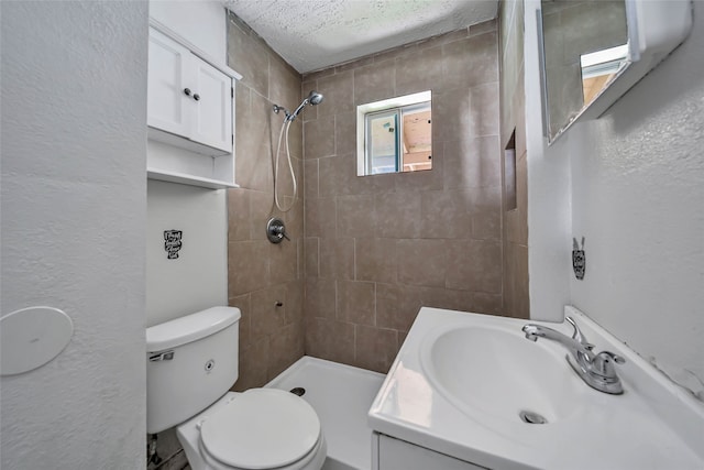 bathroom with vanity, a tile shower, a textured ceiling, and toilet