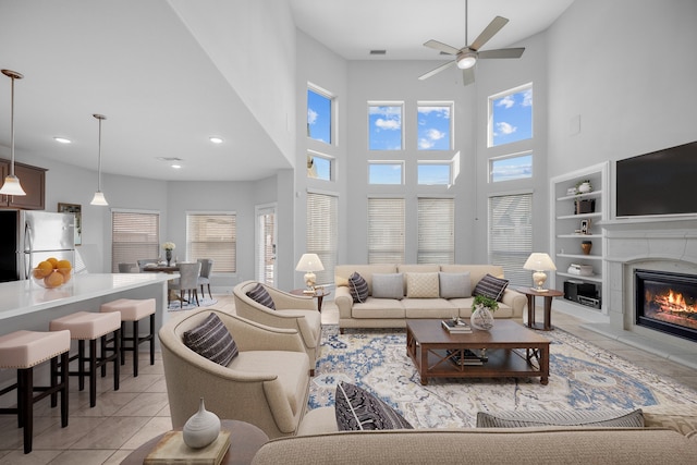 living room with ceiling fan, built in shelves, a towering ceiling, and light tile patterned floors