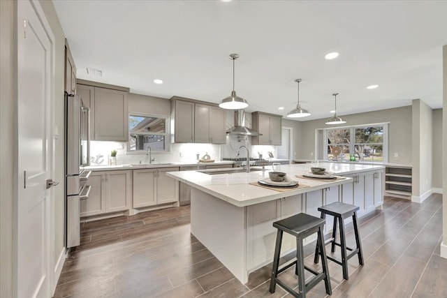 kitchen featuring dark hardwood / wood-style flooring, wall chimney range hood, high end fridge, and a kitchen island with sink