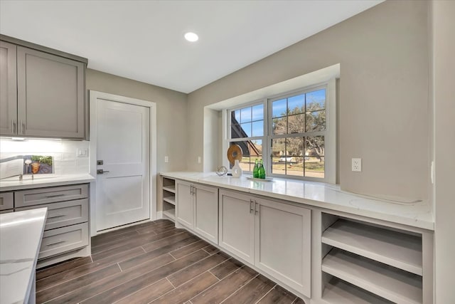 kitchen featuring dark wood-type flooring, light stone countertops, gray cabinetry, and tasteful backsplash