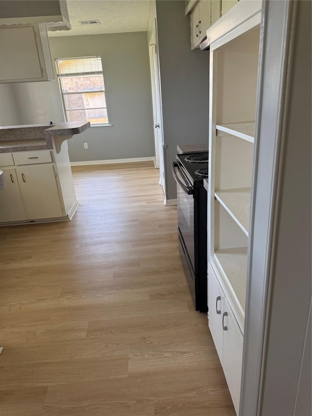 kitchen featuring dark countertops, visible vents, black range with electric stovetop, light wood-style flooring, and baseboards