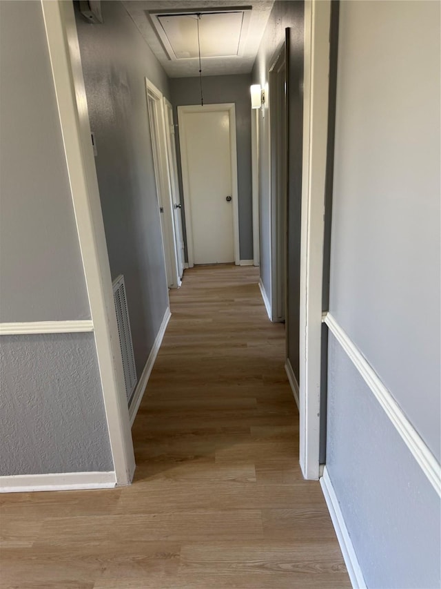 hall featuring light wood finished floors, attic access, visible vents, and baseboards