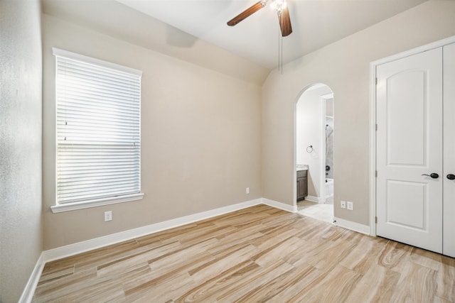 unfurnished bedroom with multiple windows, ensuite bath, light wood-type flooring, and ceiling fan