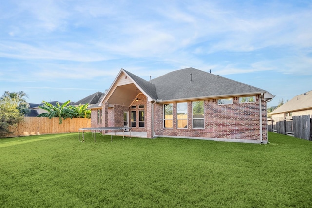 rear view of property with a trampoline and a lawn