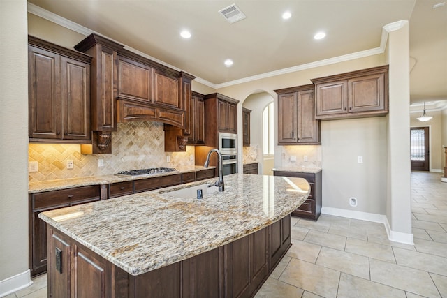 kitchen with light stone countertops, appliances with stainless steel finishes, sink, and an island with sink