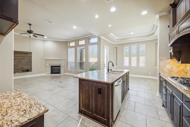 kitchen with an island with sink, stainless steel appliances, sink, light stone countertops, and tasteful backsplash