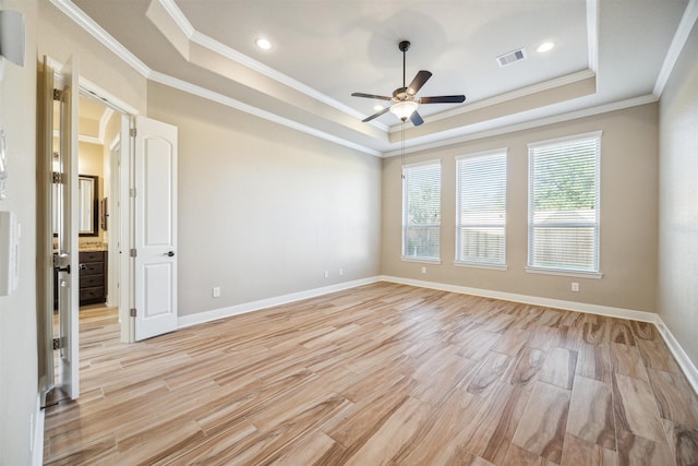 empty room with ornamental molding, light hardwood / wood-style flooring, ceiling fan, and a raised ceiling