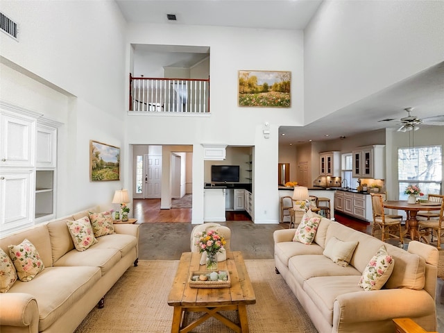 living room with dark wood-type flooring, ceiling fan, and a high ceiling