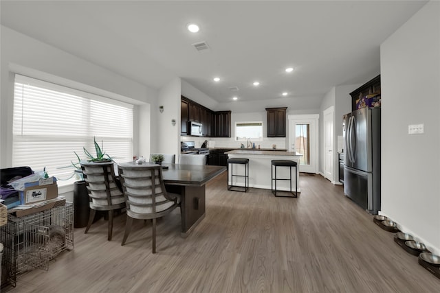 kitchen with appliances with stainless steel finishes, sink, a center island, a kitchen breakfast bar, and hardwood / wood-style flooring