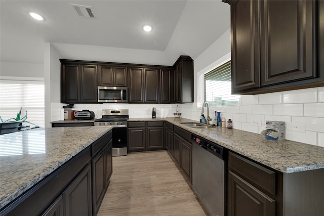 kitchen with decorative backsplash, appliances with stainless steel finishes, vaulted ceiling, light hardwood / wood-style flooring, and sink