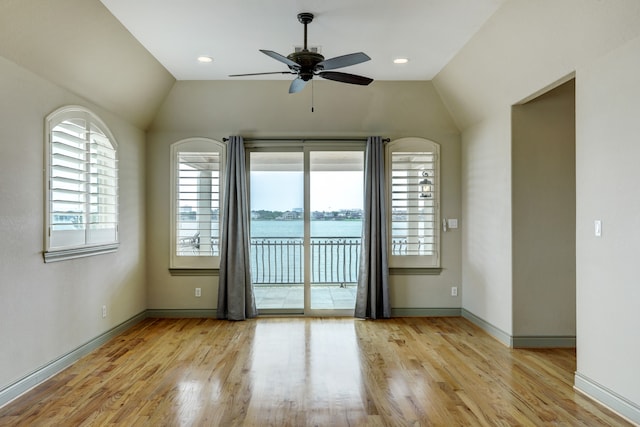 unfurnished room with lofted ceiling, a water view, light wood-type flooring, and ceiling fan