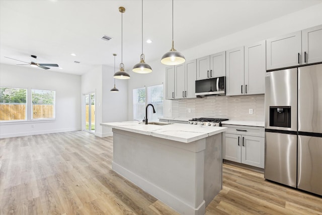 kitchen with a healthy amount of sunlight, light stone countertops, stainless steel appliances, and hanging light fixtures