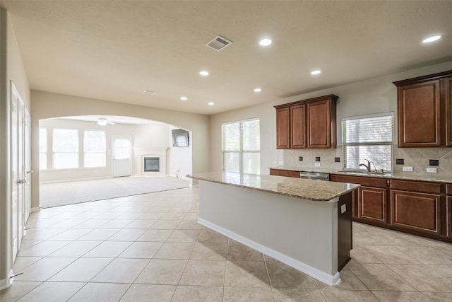 kitchen featuring backsplash, light stone countertops, a center island, light tile patterned flooring, and ceiling fan