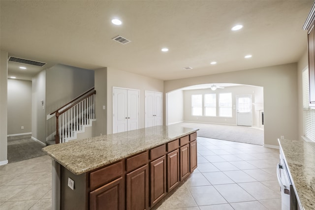 kitchen with a kitchen island, light stone countertops, light colored carpet, and ceiling fan