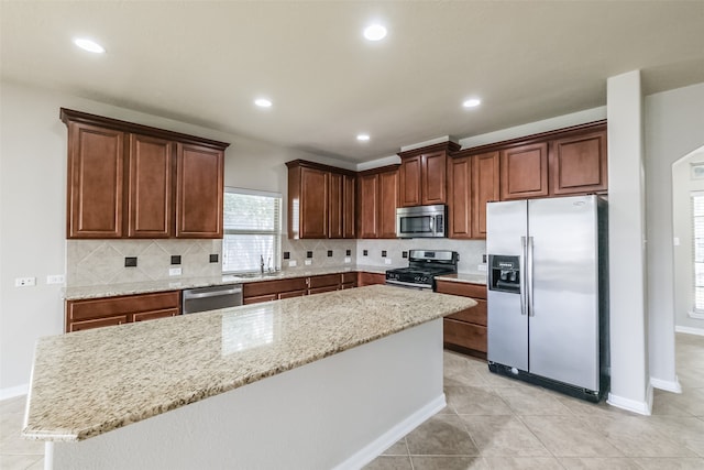 kitchen featuring backsplash, stainless steel appliances, light stone countertops, and a kitchen island