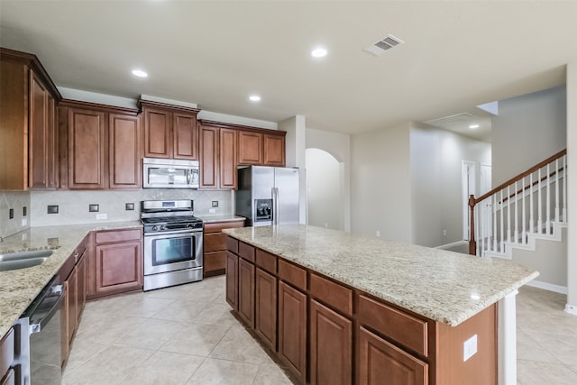 kitchen with light tile patterned floors, backsplash, a kitchen island, stainless steel appliances, and light stone counters