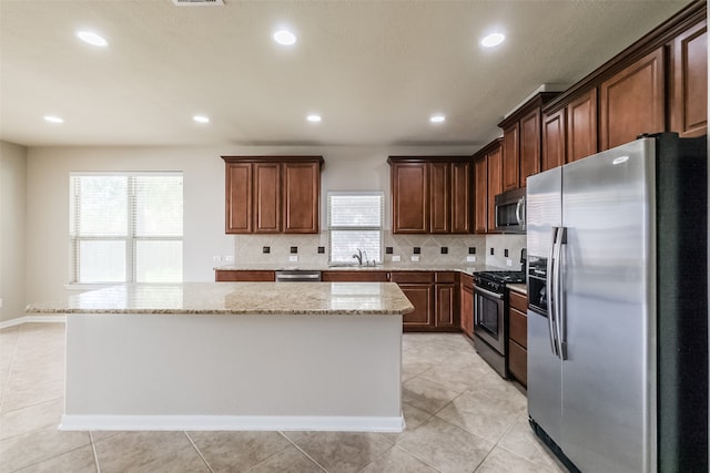 kitchen featuring stainless steel appliances, sink, a center island, light stone counters, and tasteful backsplash