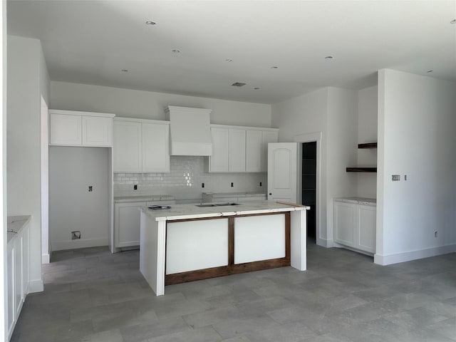 kitchen with white cabinets, custom range hood, backsplash, and an island with sink