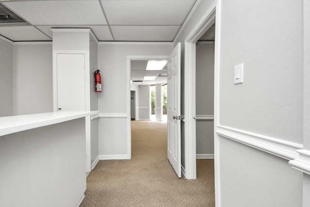 hall with a paneled ceiling and light colored carpet