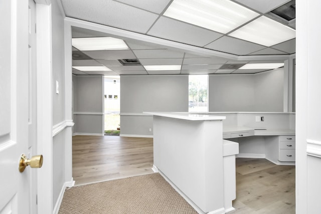 unfurnished office featuring a paneled ceiling, built in desk, and light wood-type flooring