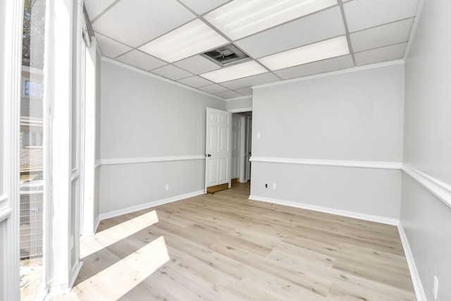 empty room featuring ornamental molding, a paneled ceiling, and light wood-type flooring