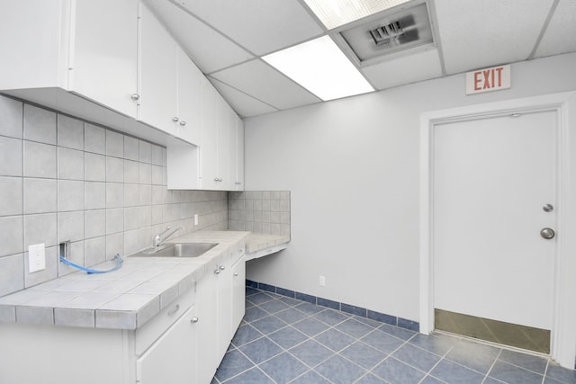 kitchen featuring a drop ceiling, white cabinetry, and backsplash