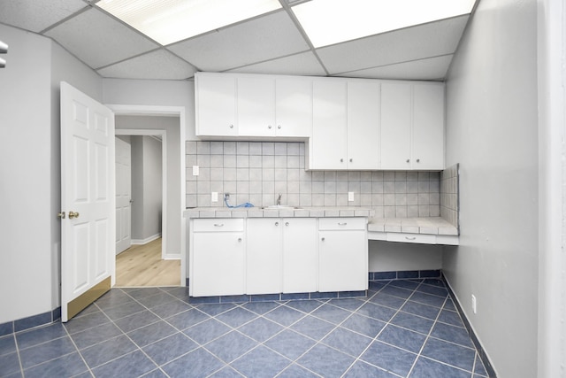 kitchen with dark tile patterned flooring, white cabinets, a paneled ceiling, and tasteful backsplash