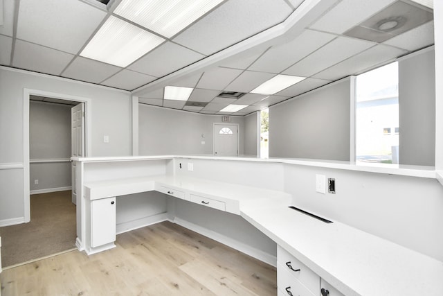 unfurnished office featuring a paneled ceiling, built in desk, and light wood-type flooring