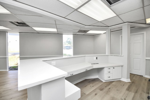 unfurnished office with built in desk, a drop ceiling, and light wood-type flooring