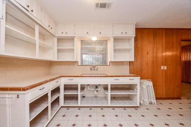 kitchen with tile counters, white cabinets, and wooden walls