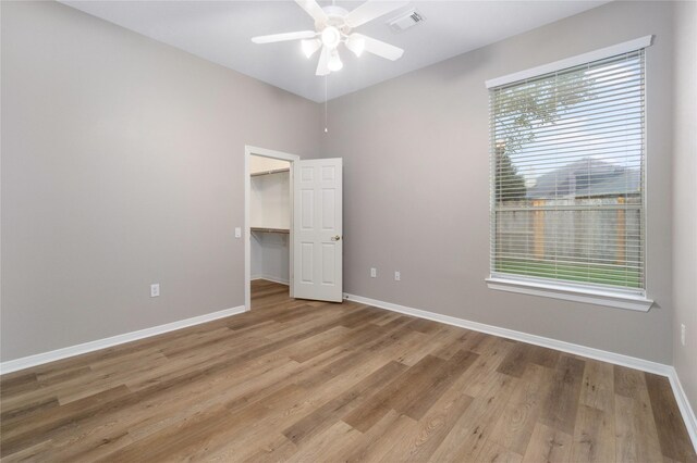 unfurnished bedroom featuring light hardwood / wood-style flooring, multiple windows, a spacious closet, and ceiling fan