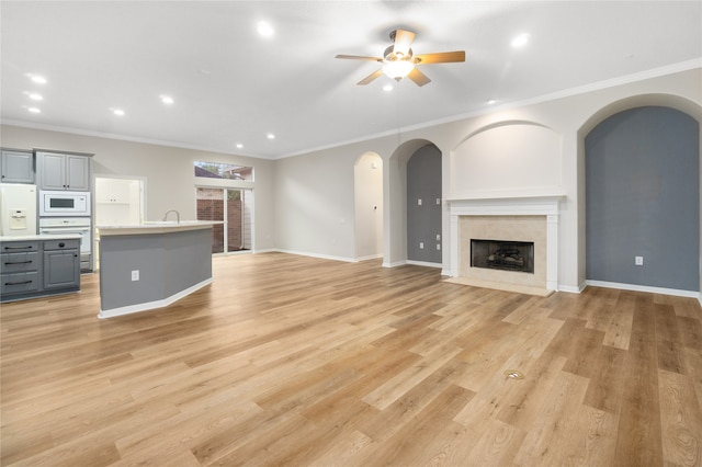 unfurnished living room with light hardwood / wood-style floors, ornamental molding, and ceiling fan