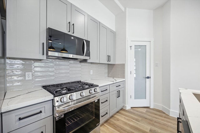 kitchen featuring light stone countertops, appliances with stainless steel finishes, backsplash, ceiling fan, and light hardwood / wood-style floors