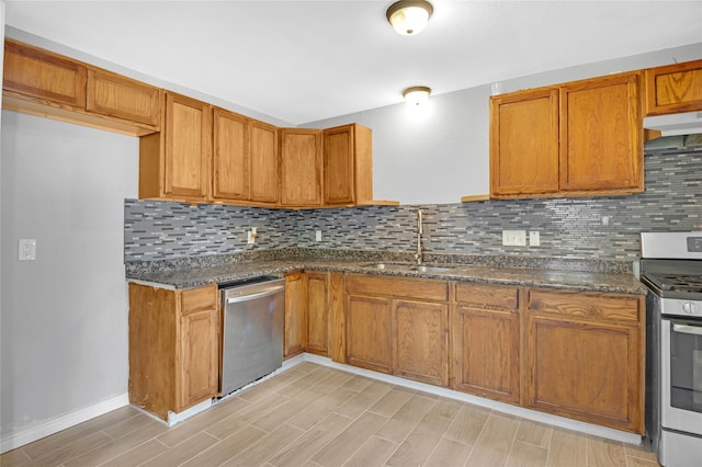 kitchen featuring dark stone counters, sink, light wood-type flooring, appliances with stainless steel finishes, and tasteful backsplash