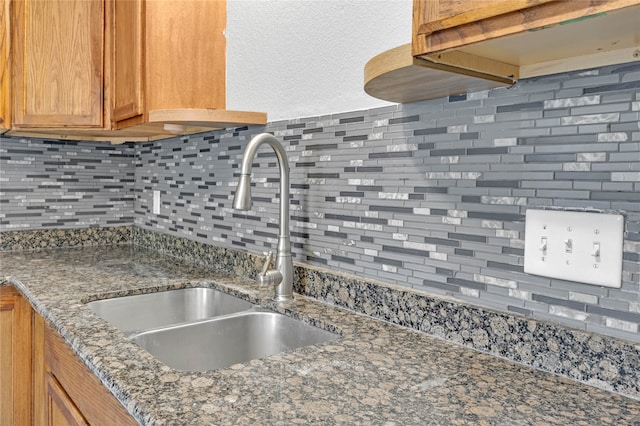 kitchen with tasteful backsplash, dark stone countertops, and sink