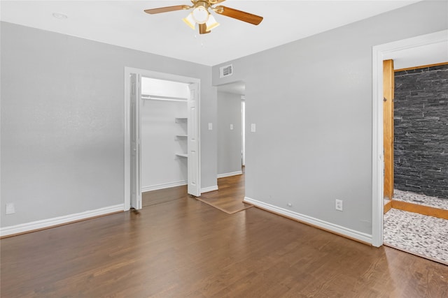 unfurnished bedroom featuring ceiling fan, a walk in closet, and dark wood-type flooring