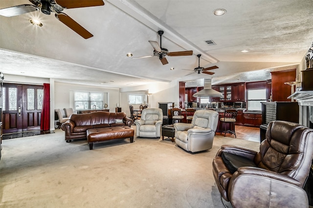 carpeted living room with a textured ceiling, vaulted ceiling with beams, a fireplace, and ceiling fan