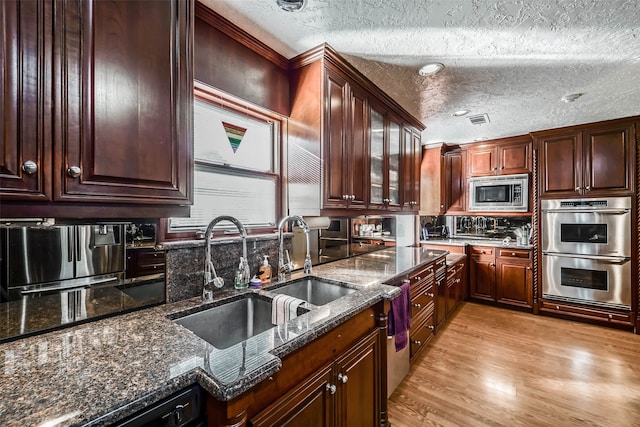 kitchen featuring appliances with stainless steel finishes, a textured ceiling, sink, and light hardwood / wood-style floors