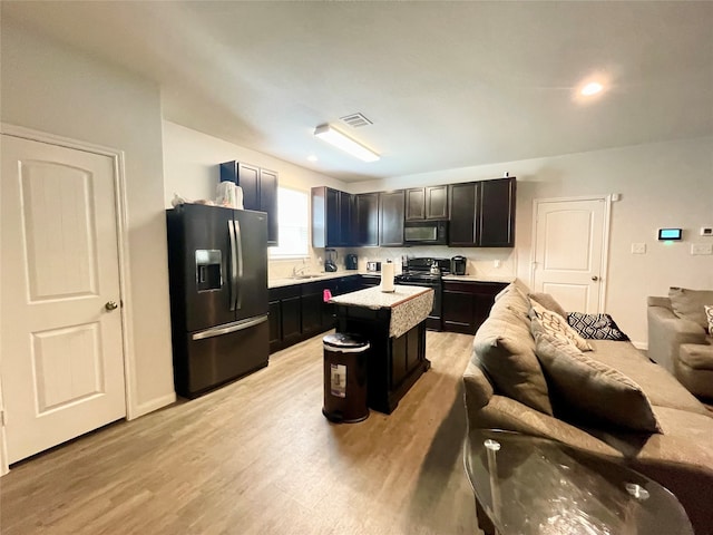 kitchen featuring black appliances, light hardwood / wood-style floors, light stone counters, and a kitchen island