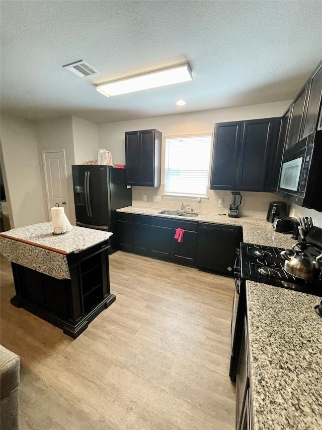 kitchen with a kitchen island, light hardwood / wood-style flooring, sink, black appliances, and a textured ceiling