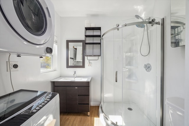 bathroom with hardwood / wood-style floors, vanity, stacked washing maching and dryer, and a shower with shower door