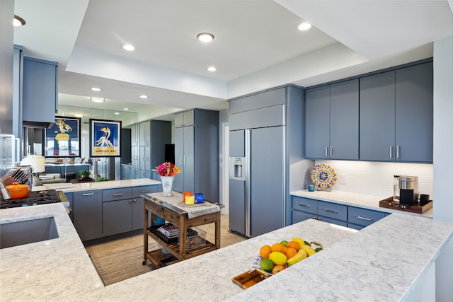 kitchen featuring blue cabinets, decorative backsplash, paneled built in refrigerator, and a tray ceiling