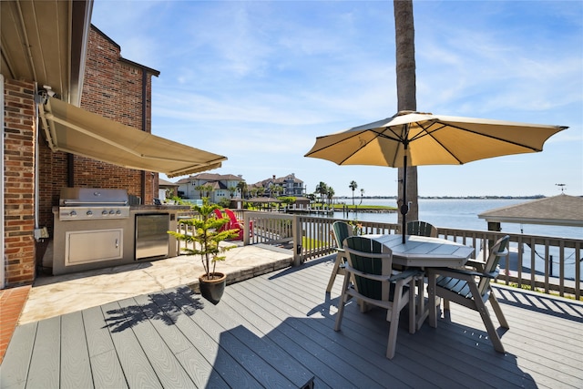 wooden deck featuring a water view, a grill, and exterior kitchen