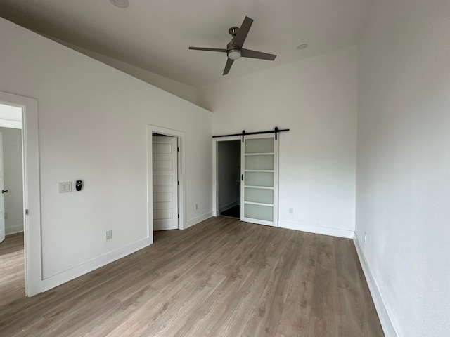 unfurnished bedroom with a closet, a barn door, light wood-type flooring, and ceiling fan