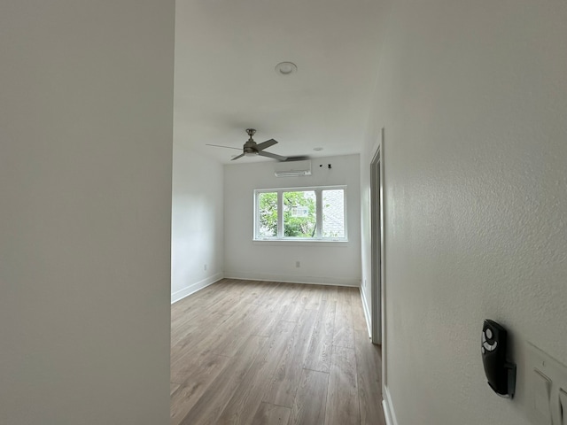 empty room featuring light hardwood / wood-style floors, a wall mounted AC, and ceiling fan