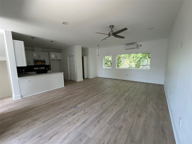 unfurnished living room with an AC wall unit, light hardwood / wood-style flooring, and ceiling fan