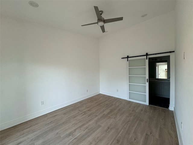 spare room with ceiling fan, a barn door, and hardwood / wood-style floors