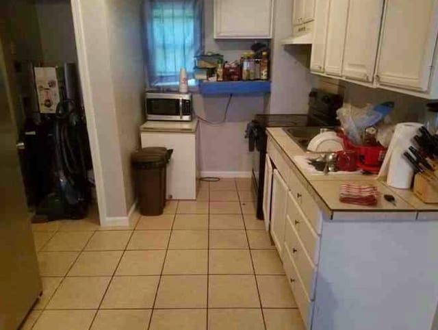 kitchen with electric range, light tile patterned flooring, and white cabinets