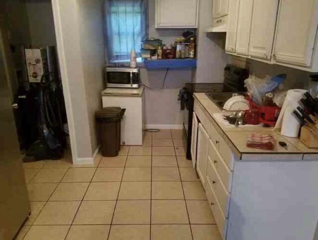 6516 Sidney St Unit A, Houston, TX 77021 - kitchen with black range with electric cooktop, stainless steel microwave, light tile patterned floors, and white cabinets