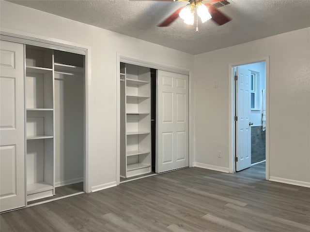 unfurnished bedroom featuring ceiling fan, a textured ceiling, two closets, and dark hardwood / wood-style floors